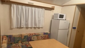 A compact kitchenette with a refrigerator, a microwave, a small table, and a sofa with a colorful pattern. - Mobile Home au Ranch du Bonheur, Évasion à la Ferme (Tourtouse)