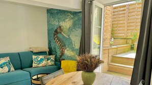 Una sala de estar con un sofá azul verdoso, un otoman amarillo y una mesa redonda de madera con un jarrón de plantas secas.