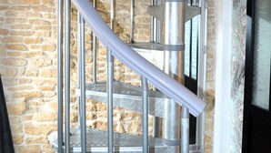 Una escalera en espiral con barandillas de metal y un fondo de pared de piedra.