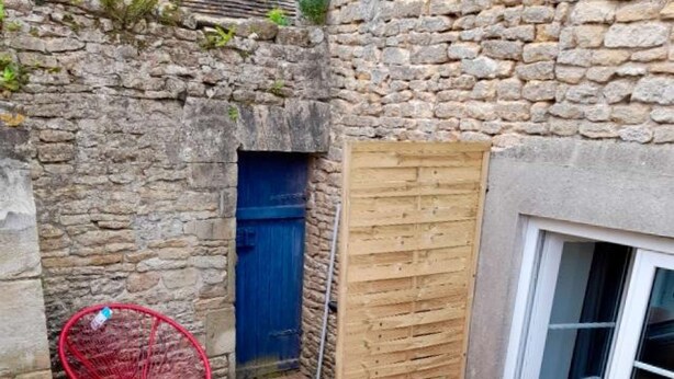 Una terraza de madera con una silla roja, una puerta azul y un panel de madera.