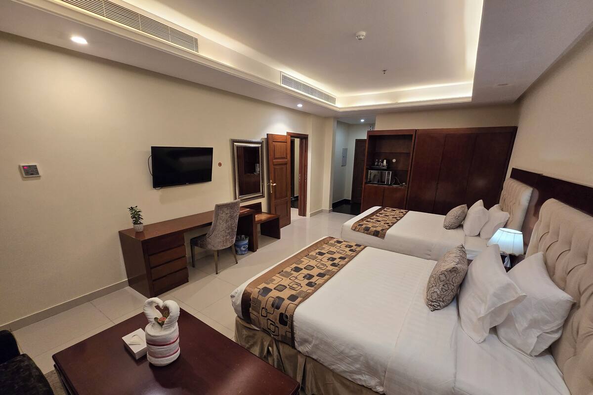 A hotel room with two beds, a desk, a chair, a TV, and a minibar.