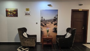 Un vestíbulo con dos sillones, una mesa con un florero, un cuadro y una puerta con el símbolo de número.