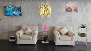 Un hall con dos sillones color crema, una pequeña mesa con una flor rosa, un televisor montado en la pared y un letrero de bienvenida.