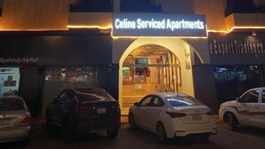 Um edifício com uma placa indicando "Celine Serviced Apartments" e outra placa com "e Expert Trading Co". Há carros estacionados na frente.
