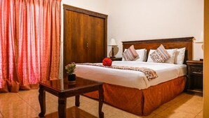 Quarto de hotel com uma cama grande, uma mesa de cabeceira de madeira, uma mesa com um vaso e um guarda-roupa.