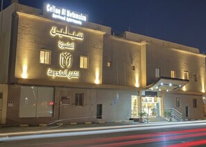 Un hôtel avec une enseigne en arabe et en anglais, une entrée couverte et un escalier bien visible menant au hall d’accueil.
