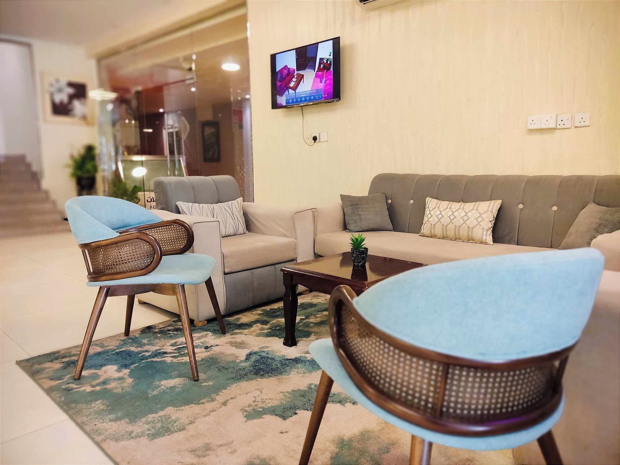 Una sala de estar con un sofá, dos sillones, una mesa de centro y un televisor de pantalla plana montado en la pared.