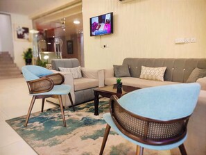 Un salon comprenant un canapé, deux fauteuils, une table basse et un téléviseur à écran plat fixé au mur.