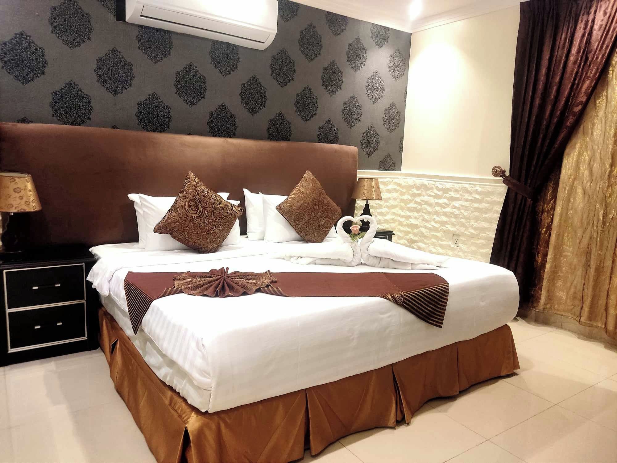 A hotel room with a large bed, a nightstand, a lamp, and a wall-mounted air conditioner.