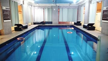 Una amplia piscina interior con agua cristalina, rodeada de sillas de descanso y una solería azulejada.