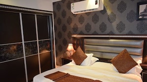 A hotel room with a large bed, a nightstand, a lamp, and a wall-mounted air conditioner. - Celine Al Motamayza Apartments (Jeddah)