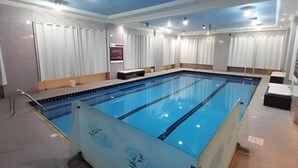 A large indoor swimming pool with clear lanes, surrounded by white curtains and a tiled floor. - Celine Al Motamayza Apartments (Jeddah)