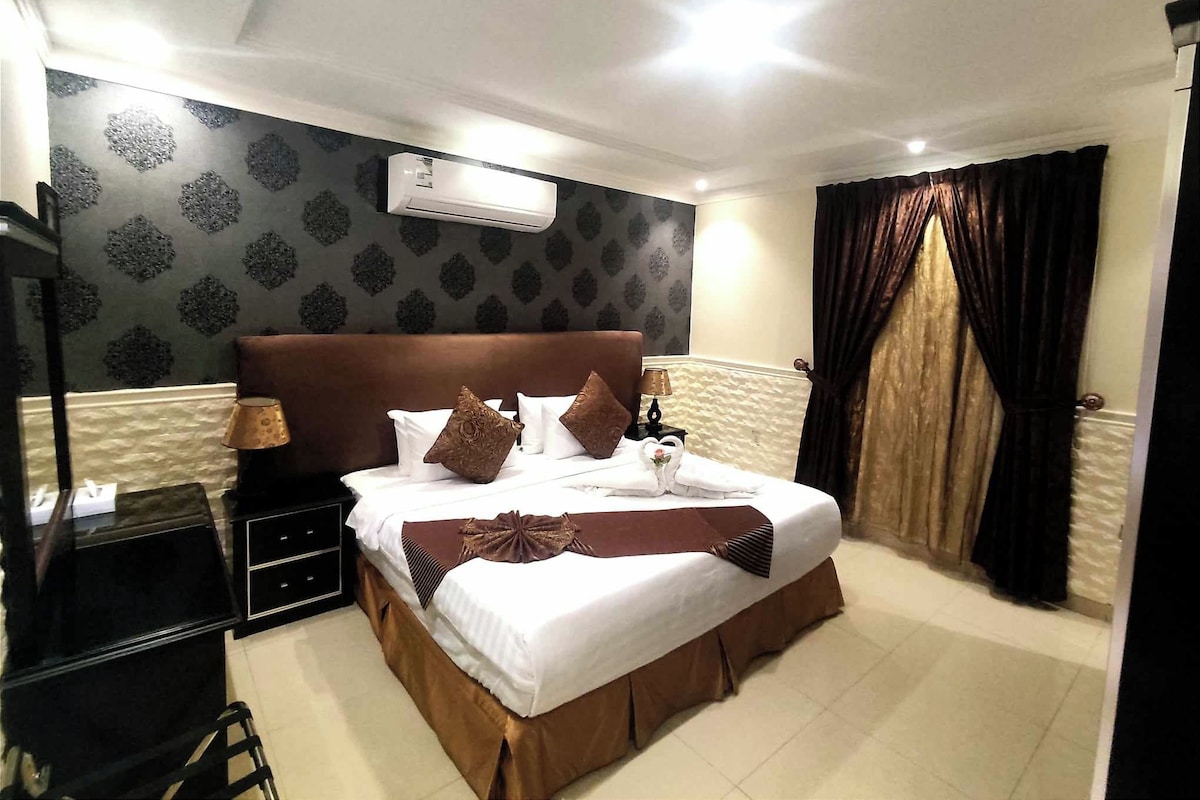 Ein Hotelzimmer mit einem großen Bett, einem Nachttisch, einer Lampe und einer Klimaanlage an der Wand.