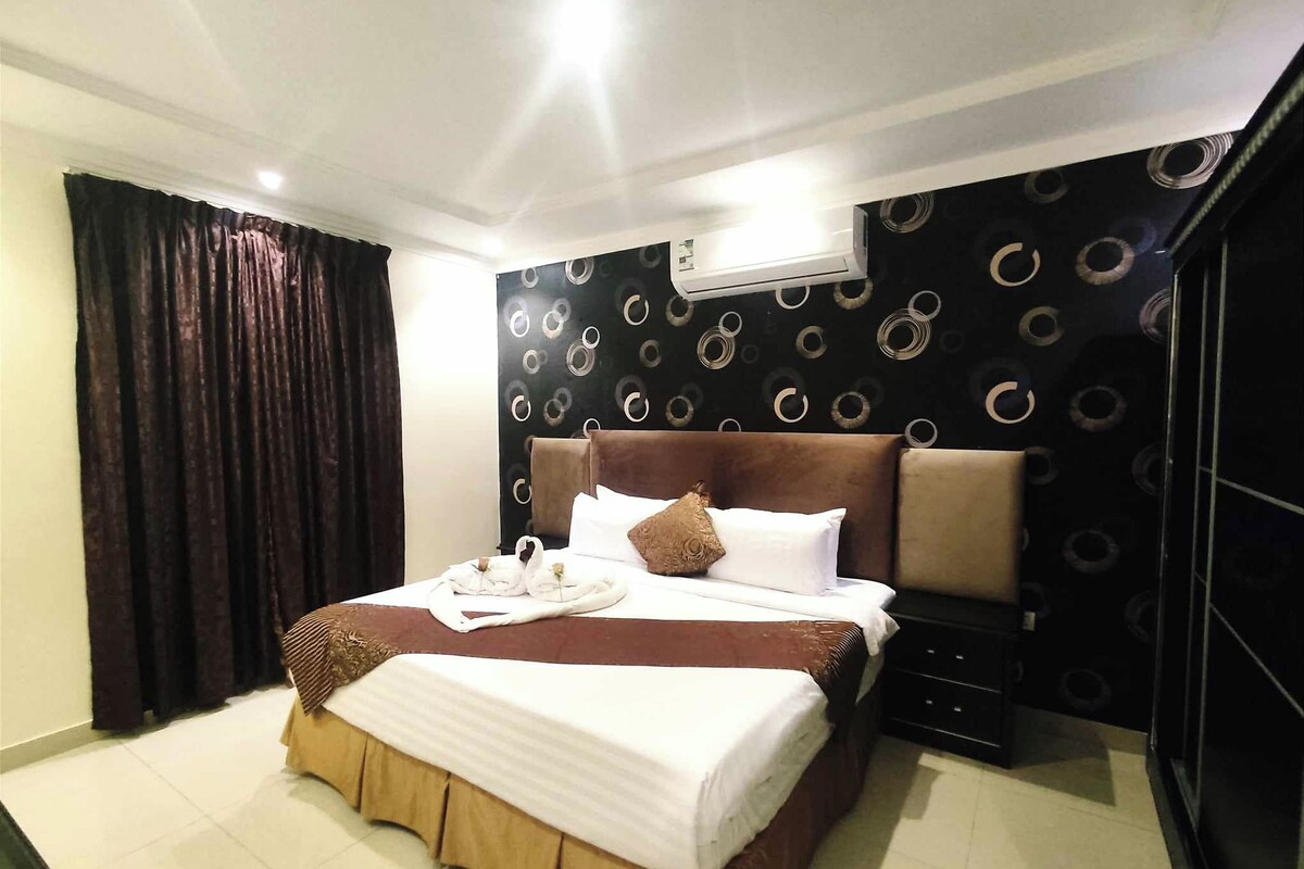 Ein Hotelzimmer mit einem großen Bett, einem Nachttisch, einer Klimaanlage und einer Wand mit dunklem Muster.