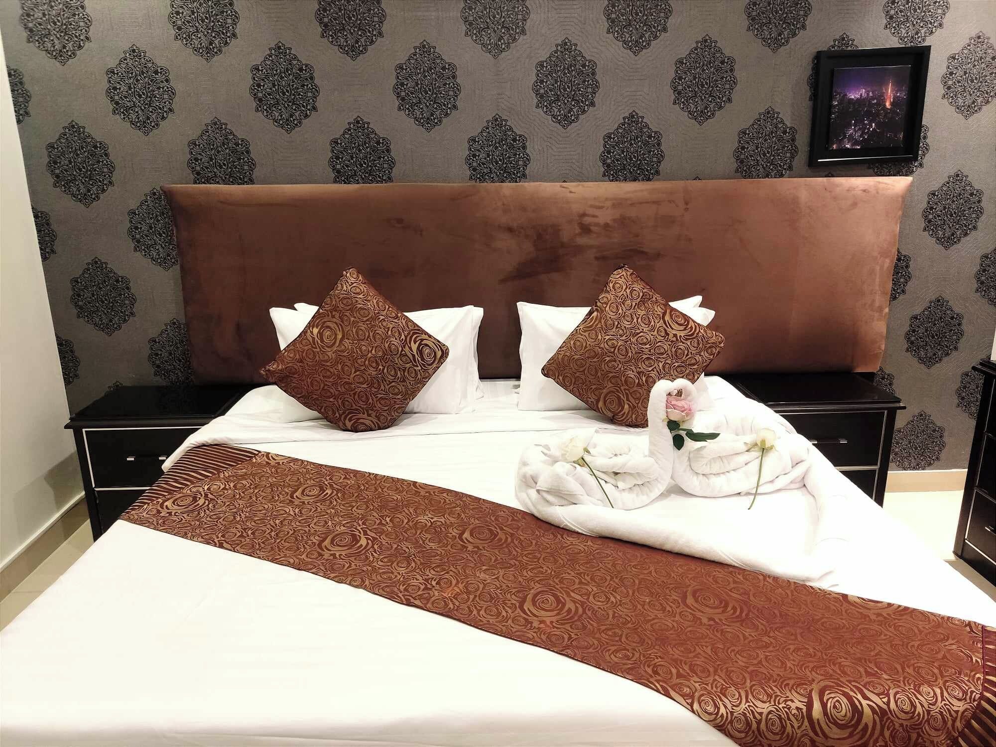 Una habitación de hotel con una cama, dos mesitas de noche, un cabecero y un cuadro enmarcado en la pared.