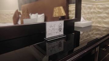 Un mostrador de recepción de hotel con una tarjeta de recepción, un espejo que refleja una cama y una lámpara, y una pared con textura al fondo.