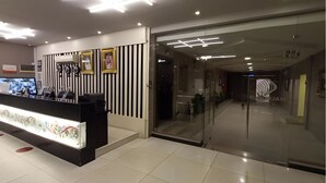 A modern reception area with a black and white striped wall, a reception desk with a decorative light, and a glass door leading to a hallway. - Celine Al Motamayza Apartments (Jeddah)