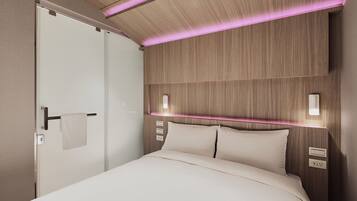 A modern hotel room with a wooden headboard, a white bed, and a door with a towel hanging on the handle.