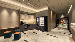 Een moderne hotellobby met een receptiebalie, een zithoek, automaten en een kinderspeelruimte.