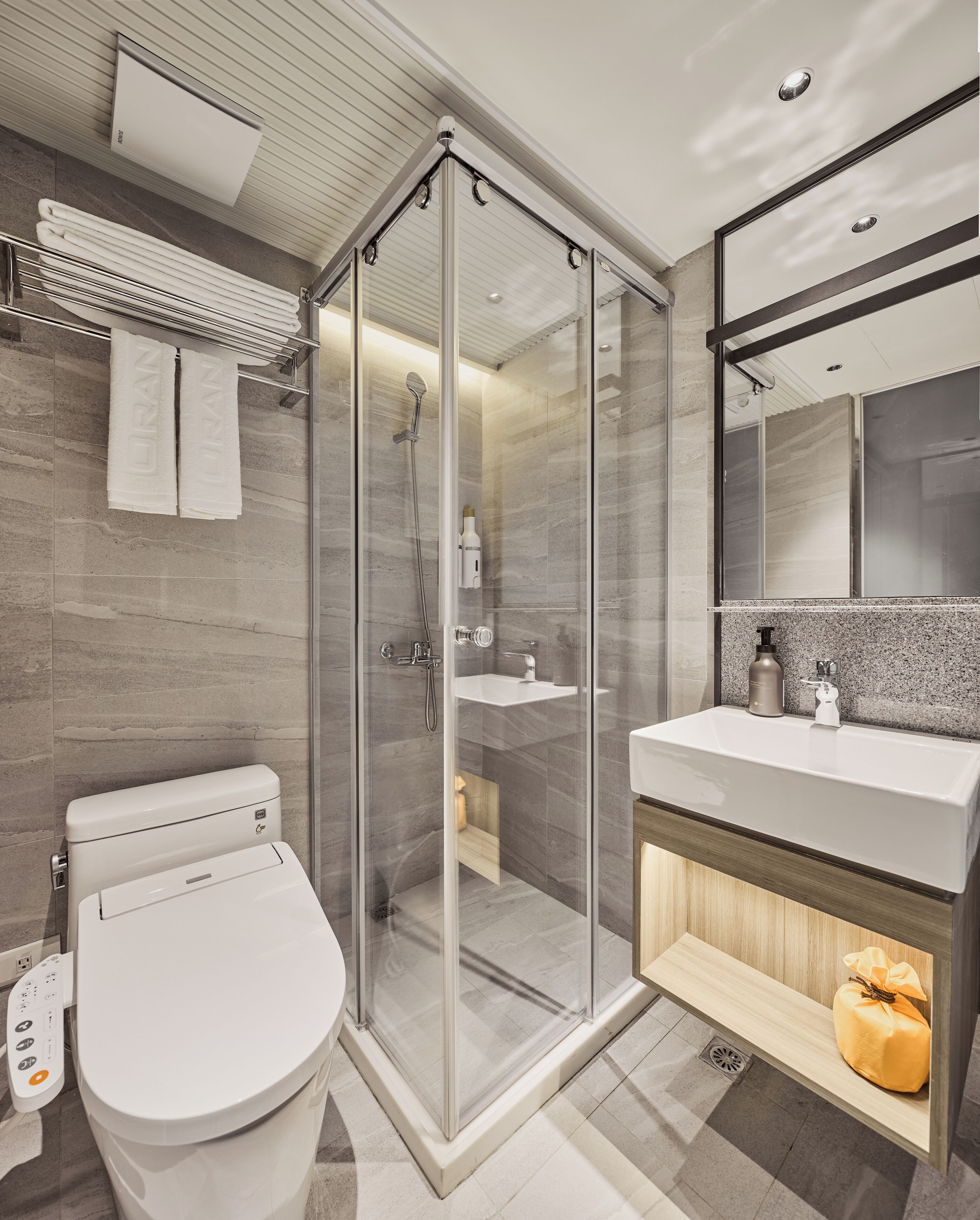 A modern bathroom with a glass-enclosed shower, a white toilet, a sink with a wooden vanity, and a mirror above the sink.