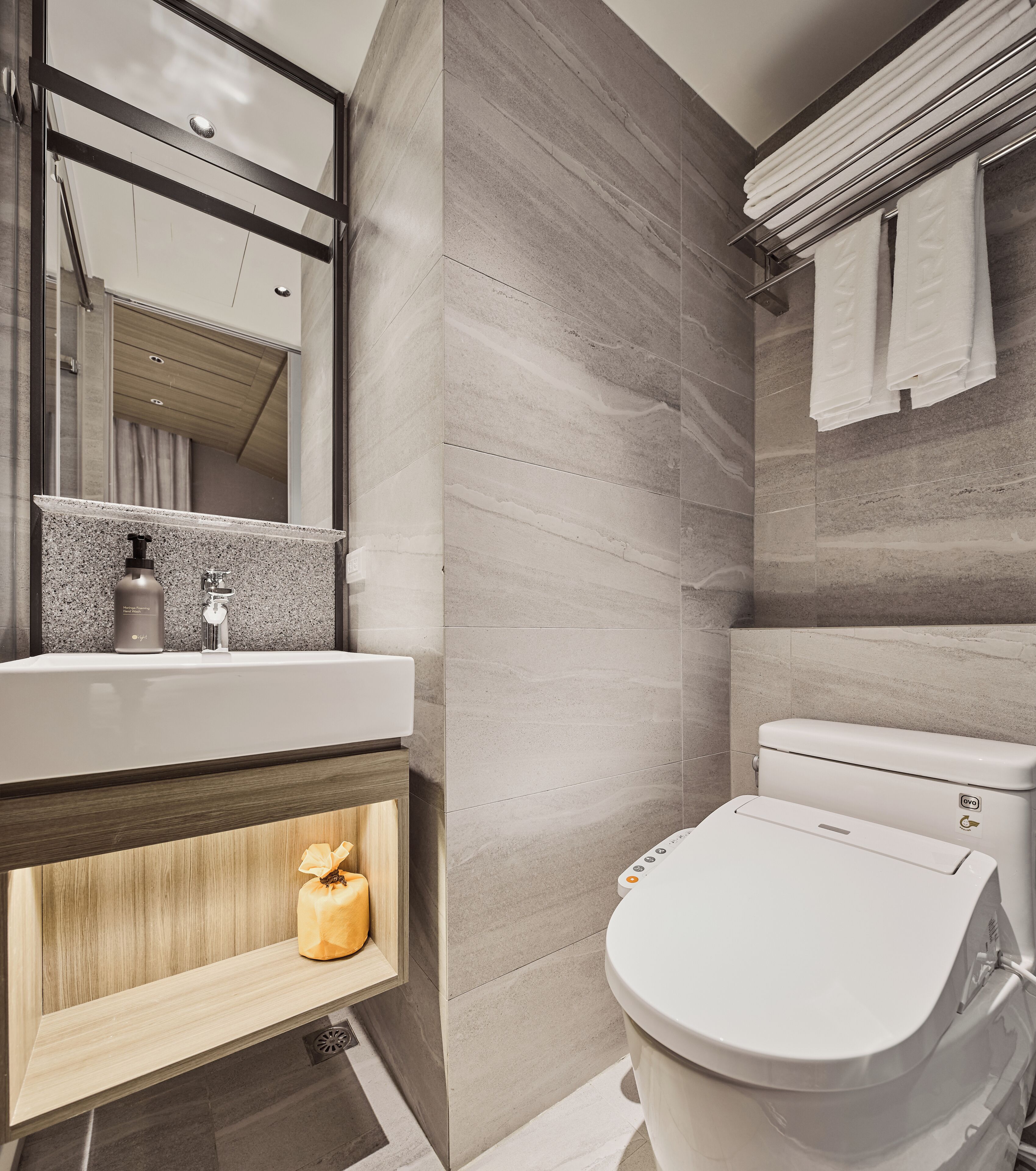 A modern bathroom with a large mirror, a sink with a soap dispenser, a toilet, and a towel rack.