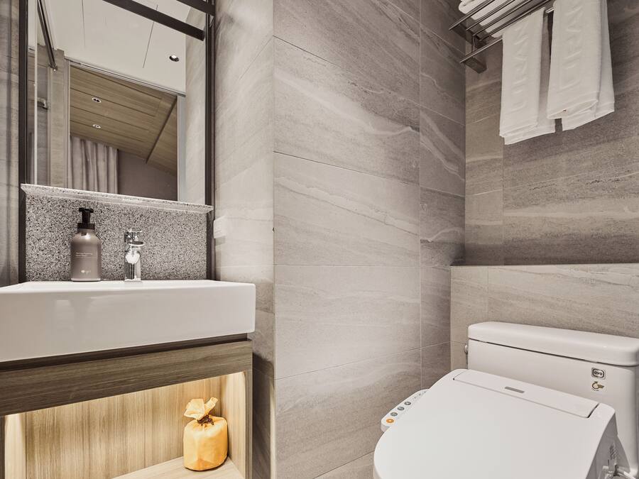 A modern bathroom with a large mirror, a sink with a soap dispenser, a toilet, and a towel rack.