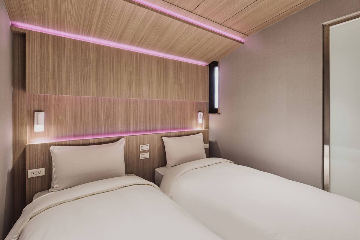 Moderni hotellihuone, jossa on kaksi sänkyä, puupanelointi ja sisäänrakennettu valaistus.