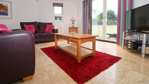 A modern living room with a leather sofa, a wooden coffee table, and a red rug. - Spacious dog friendly apartment by the beach, private garden and sea views. (Padstow)