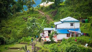 A rural house with a blue roof, surrounded by lush greenery and a steep hillside. - Nama Stay Home (Pokhara)