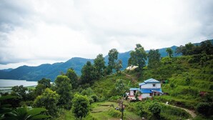 A house with a blue roof, surrounded by lush greenery and hills in the background. - Nama Stay Home (Pokhara)