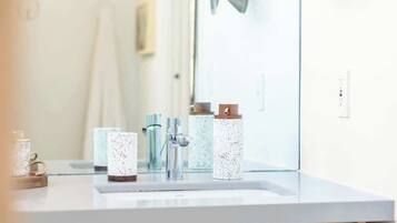 Une salle de bain avec un lavabo blanc, un miroir et trois distributeurs de savon à motifs.