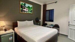 Hotelkamer met een groot bed, een bureau, een stoel, een nachtkastje, een lamp, een schilderij aan de muur en een deur.