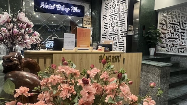Een hotel receptie met een houten balie, een neonbord met 'Hotel Đặng Ngưu' en een decoratieve bloemstelling.