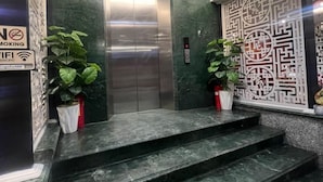 Een moderne lift met een metalen afwerking, omringd door groene marmeren wanden en decoratieve panelen.