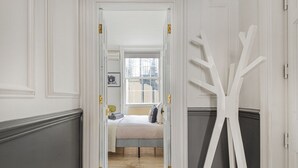 Un pasillo que conduce a un dormitorio con una cama, un ventanal y una escultura abstracta blanca.