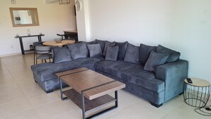 A modern living room with a grey sectional sofa, a wooden coffee table, and a round side table with a remote control. - Spacious 2-bed Apartment in Sotira With Pool (Sotira)