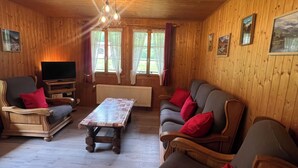 Un salón acogedor con muebles de madera, un televisor, una mesa de centro y dos sofás con cojines rojos.