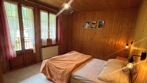 Un dormitorio de cabaña de madera con cama, mesita de noche, lámpara de pared y ventilador de techo.