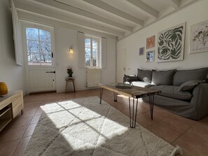 Ein geräumiges Wohnzimmer mit großem Fenster, einem grauen Sofa, einem Holztisch und einem weißen Teppich.