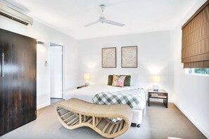 Un dormitorio con cama, mesitas de noche, ventilador de techo y ventana con persianas.