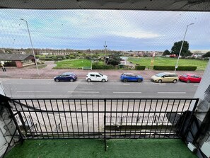 Vista desde un balcón con baranda de metal, con vistas a un estacionamiento con varios coches y un letrero verde al fondo.