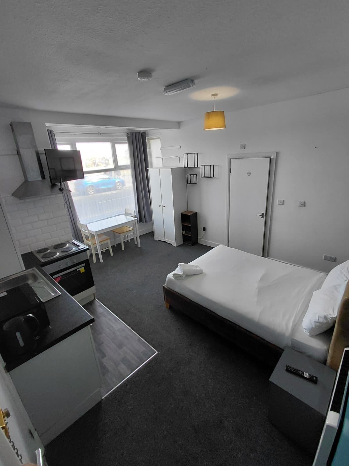 Une chambre d’hôtel compacte comprenant un coin cuisine, un lit, un bureau et une fenêtre avec des rideaux.