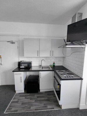 Uma cozinha compacta com armários brancos, bancada preta, micro-ondas, pia e fogão.