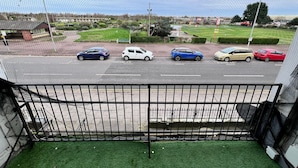 Vista desde un balcón con baranda de metal, con vistas a un estacionamiento con varios coches y un letrero verde al fondo.