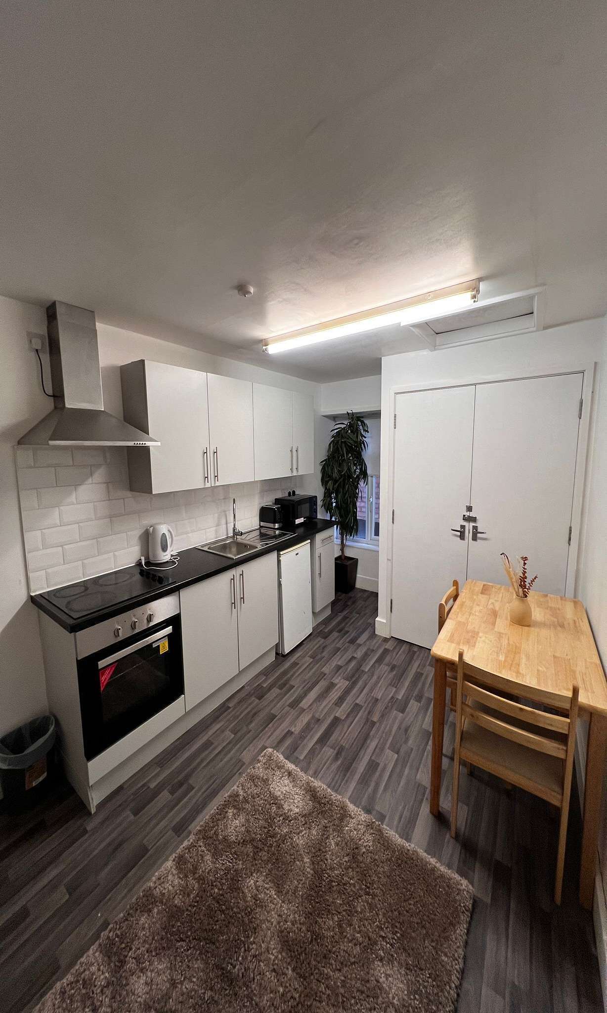 A modern kitchen with white cabinets, a black countertop, a built-in oven, and a dining area with a wooden table and chairs.
