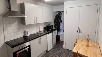 A modern kitchen with white cabinets, a black countertop, a built-in oven, and a dining area with a wooden table and chairs.