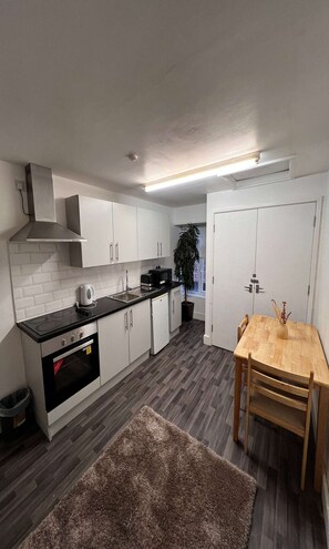 A modern kitchen with white cabinets, a black countertop, a built-in oven, and a dining area with a wooden table and chairs. - One Bedroom Apartment (Skegness)