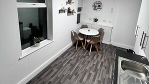 A modern kitchen with a dining area, white walls, and a grey wooden floor. - Two Bedroom - Apartment (Skegness)