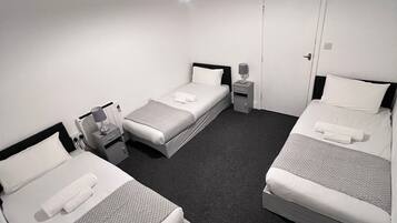 A hotel room with two single beds, a small bedside table with a lamp, a nightstand, and a door.