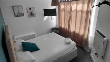Una habitación de hotel con cama, mesitas de noche, televisor y ventana con cortinas.